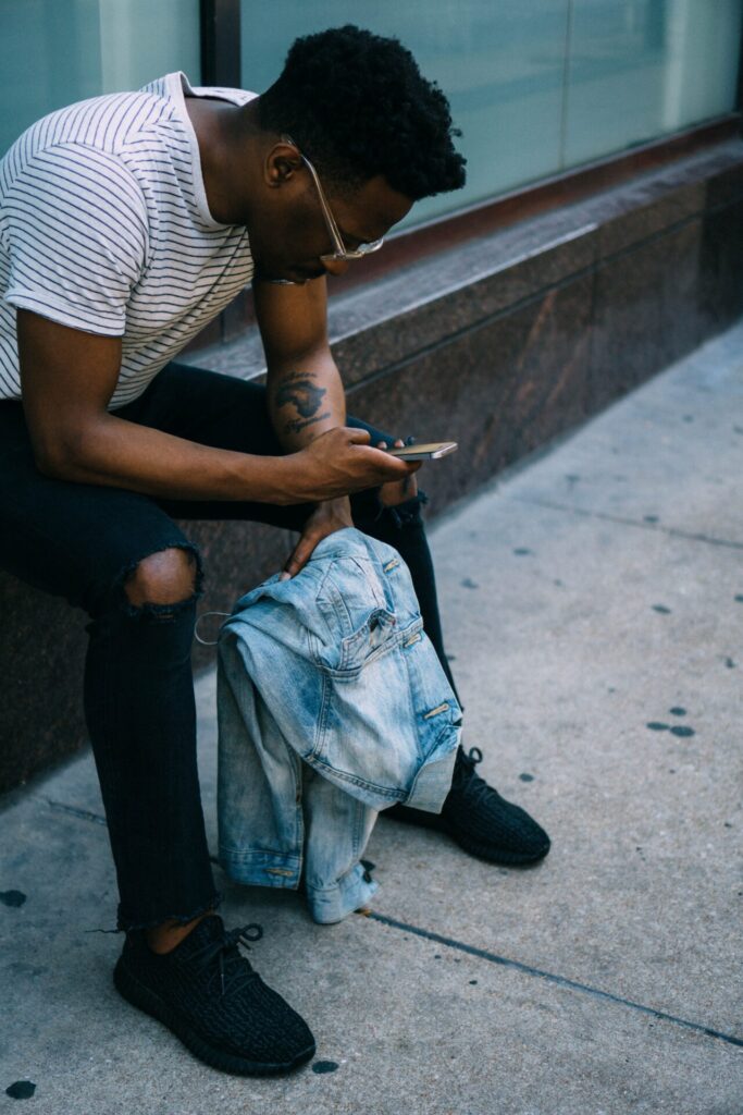 Man sitting, holding jacket and looking and mobile phone.