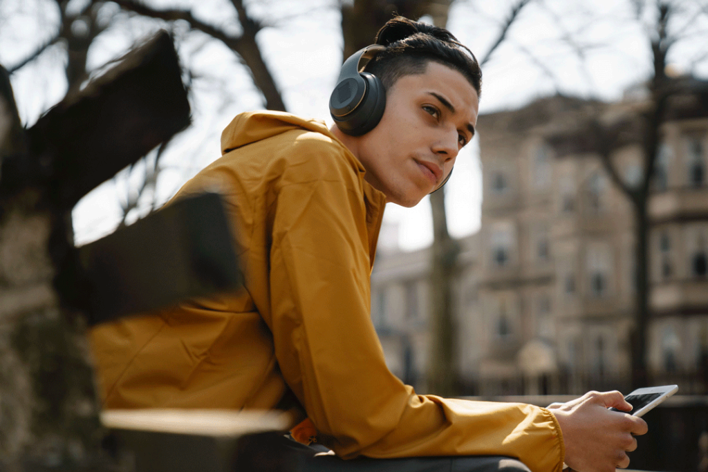 Man sitting on bench with headphones on a holding mobile phone.