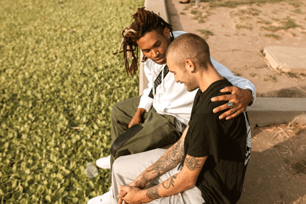 Two men sitting side by side, one man had his arm around the other.